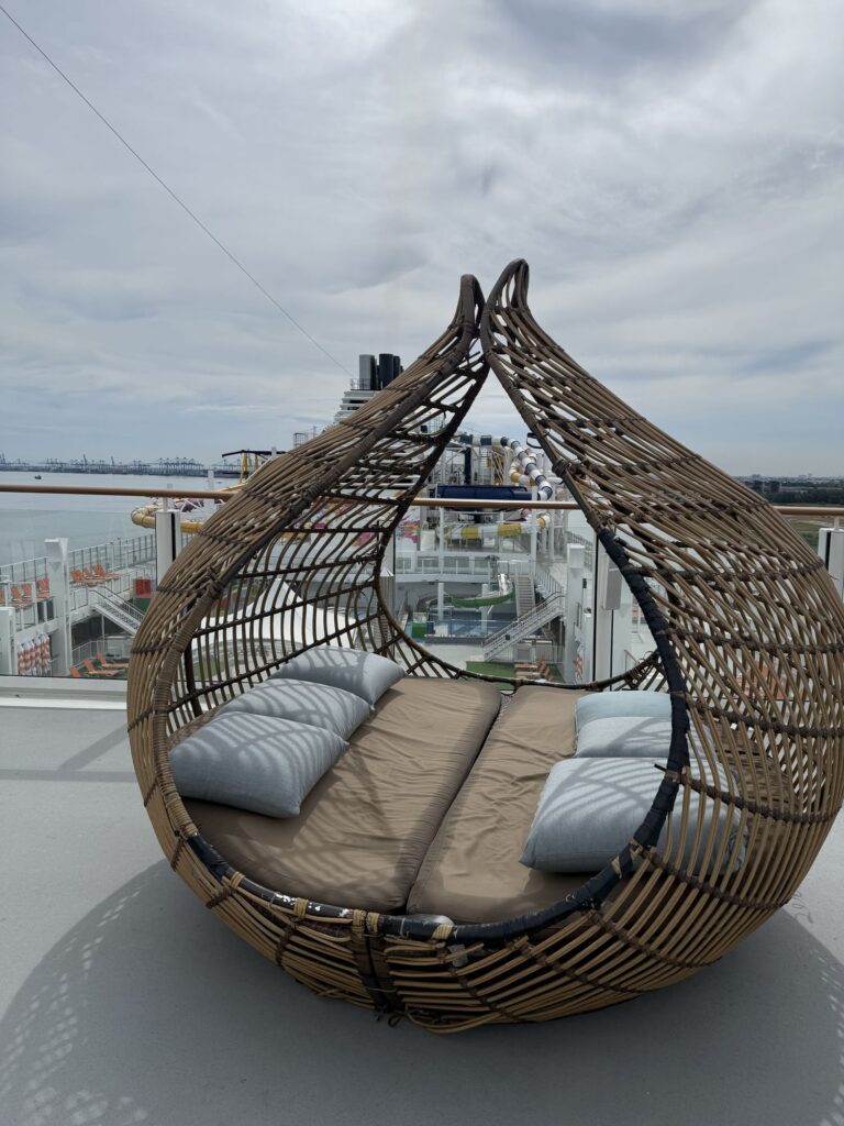 A rattan daybed on the upper deck of Genting Dream overlooking the pool deck and Port Klang harbor.