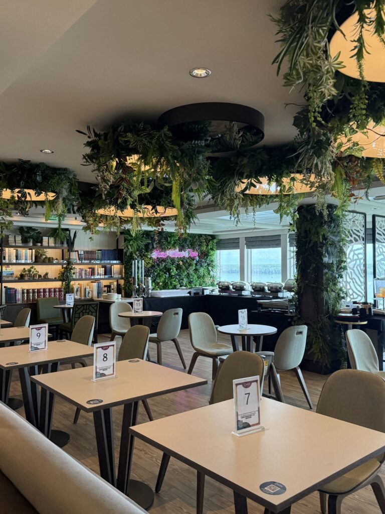 A garden-themed cafe and library venue aboard Genting Dream, with hanging plants and bookshelves.