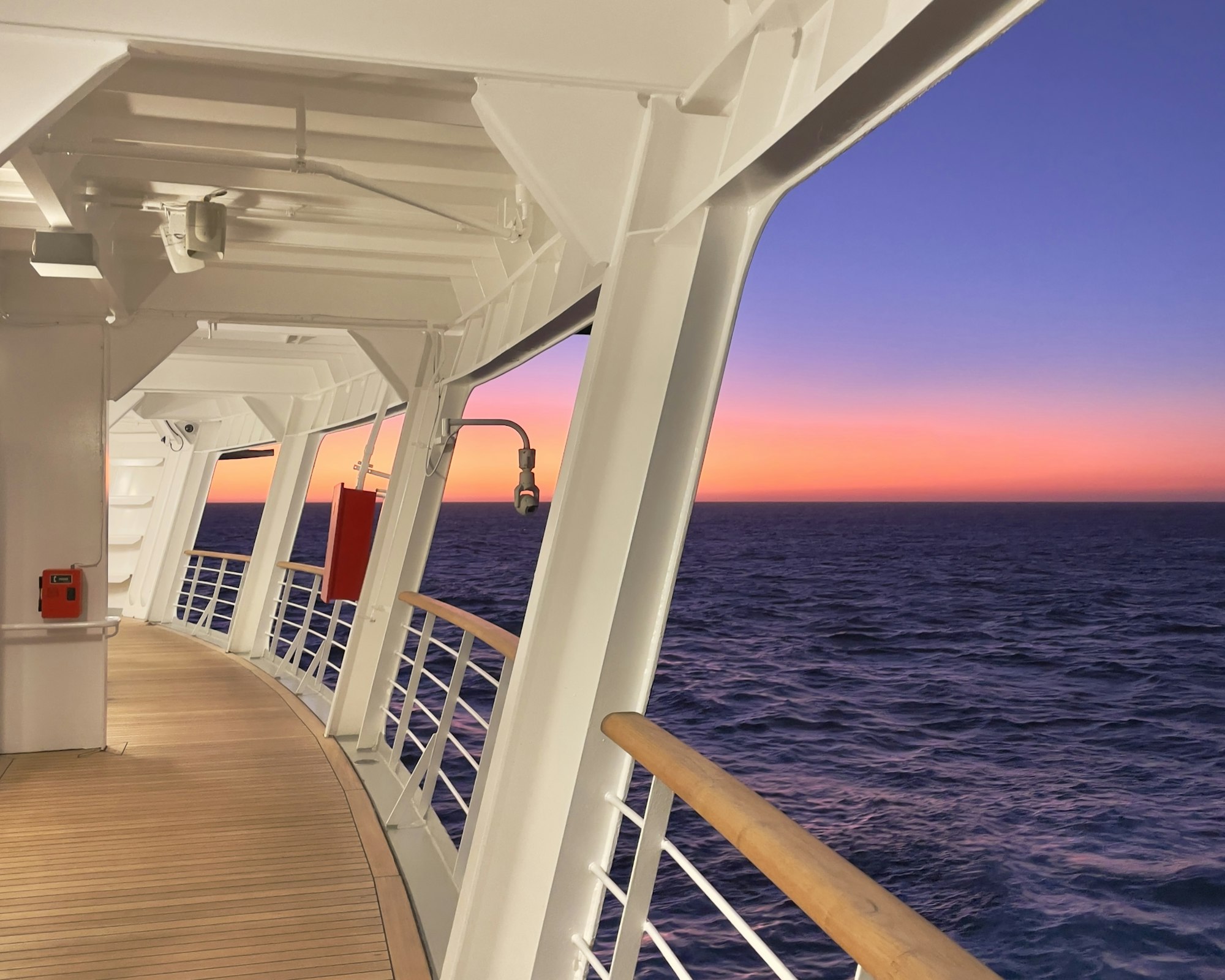 The promenade deck of a cruise ship looking out over the ocean at sunset