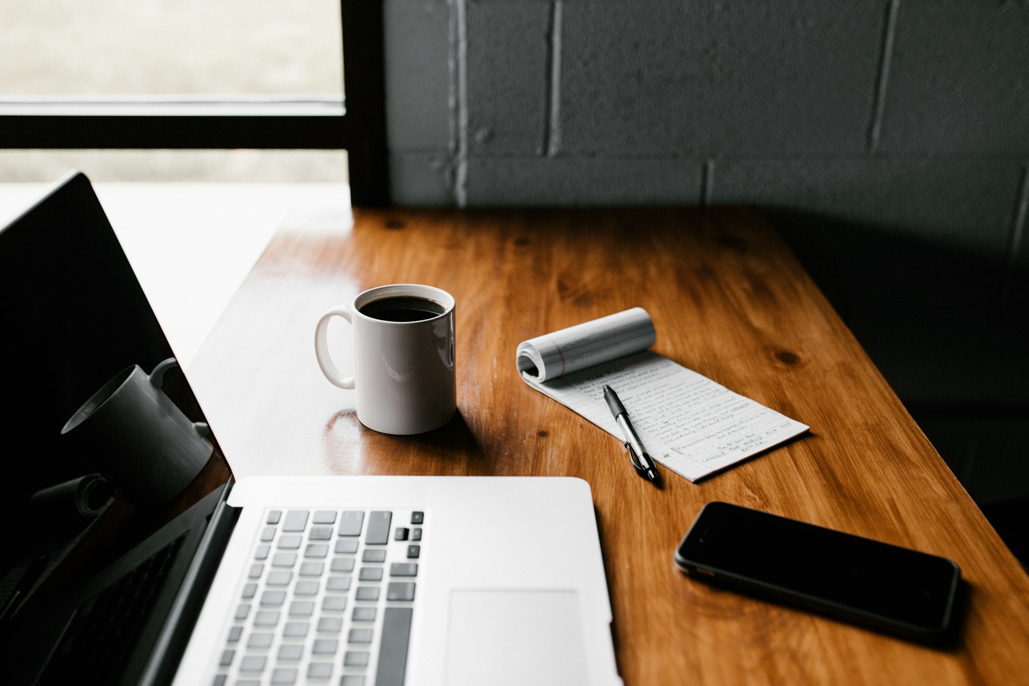 An open laptop, coffee and notepad on a desk while preparing a job application
