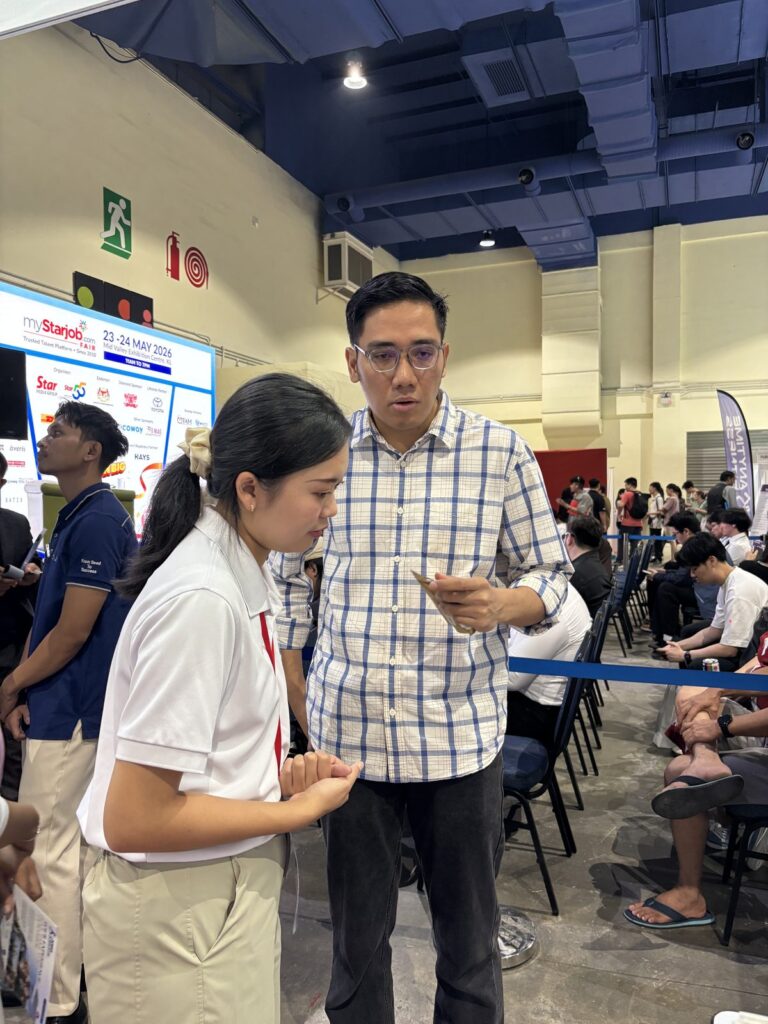 A Jobs Kreate consultant speaking with a jobseeker reading a Jobs Kreate flyer at Booth A30 during myStarjob Fair 2026, with the event screen in the background.